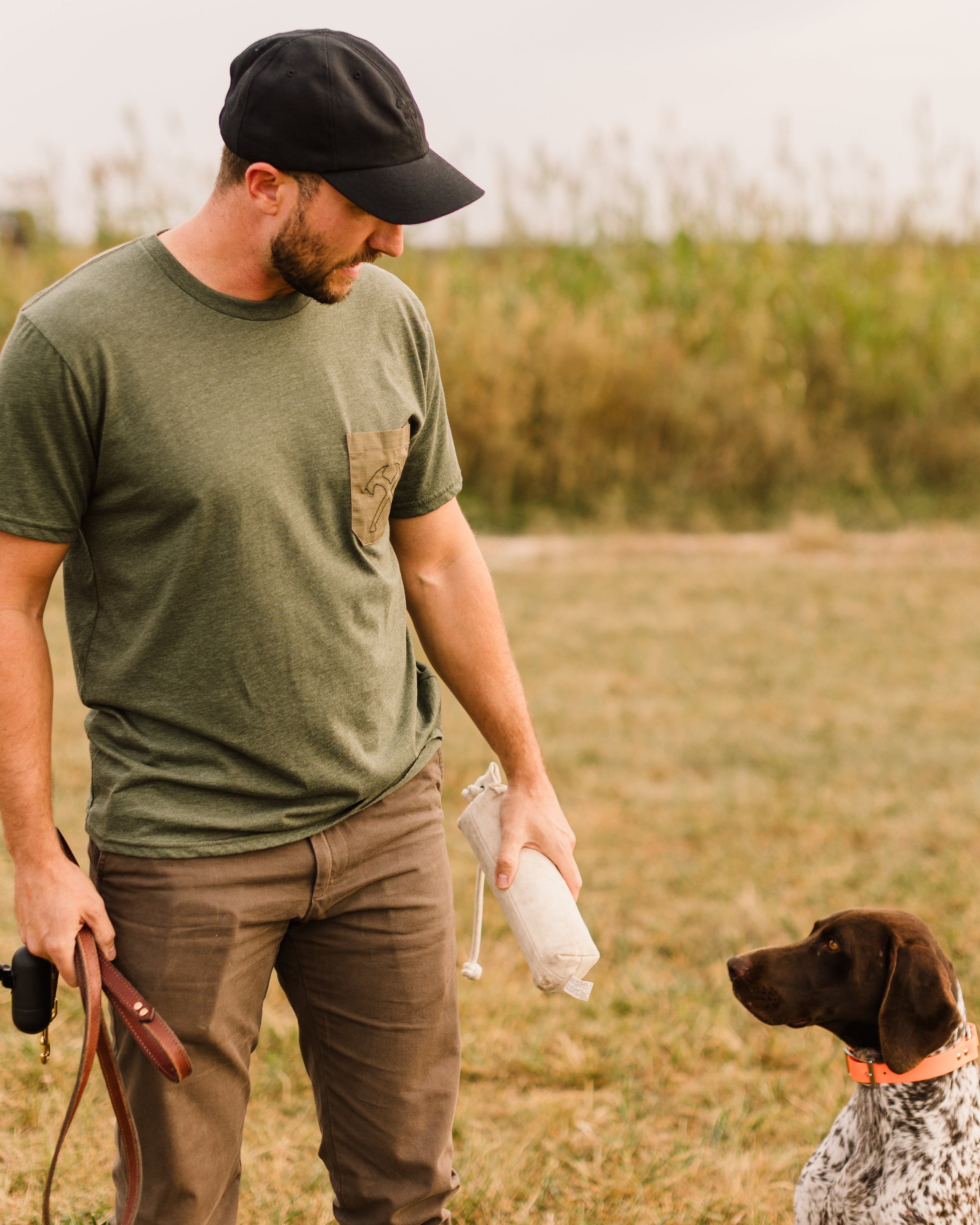 Man in a green shirt and cap standing with a dog in a field
