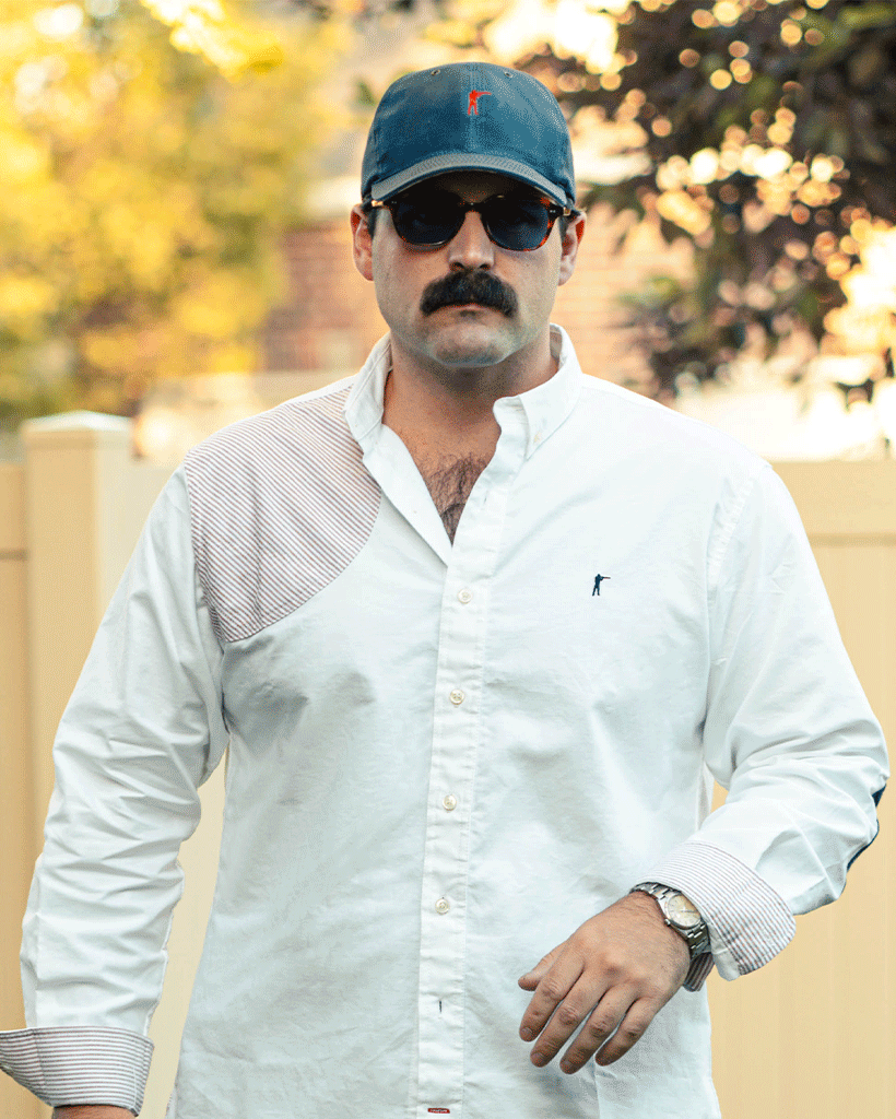 Man wearing a white shirt with a blue cap and sunglasses outdoors