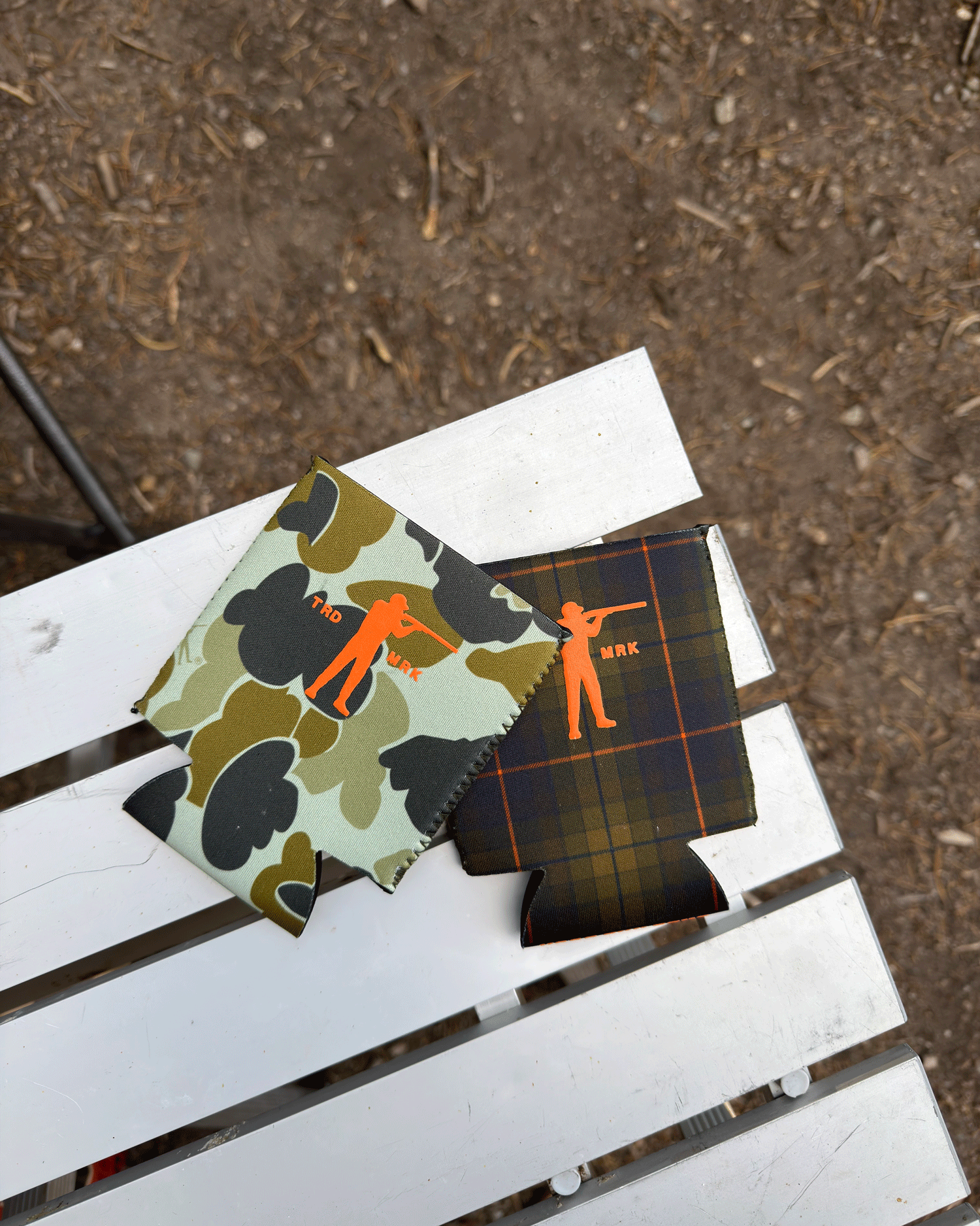 Two can coolers with camouflage and plaid patterns on a white surface.
