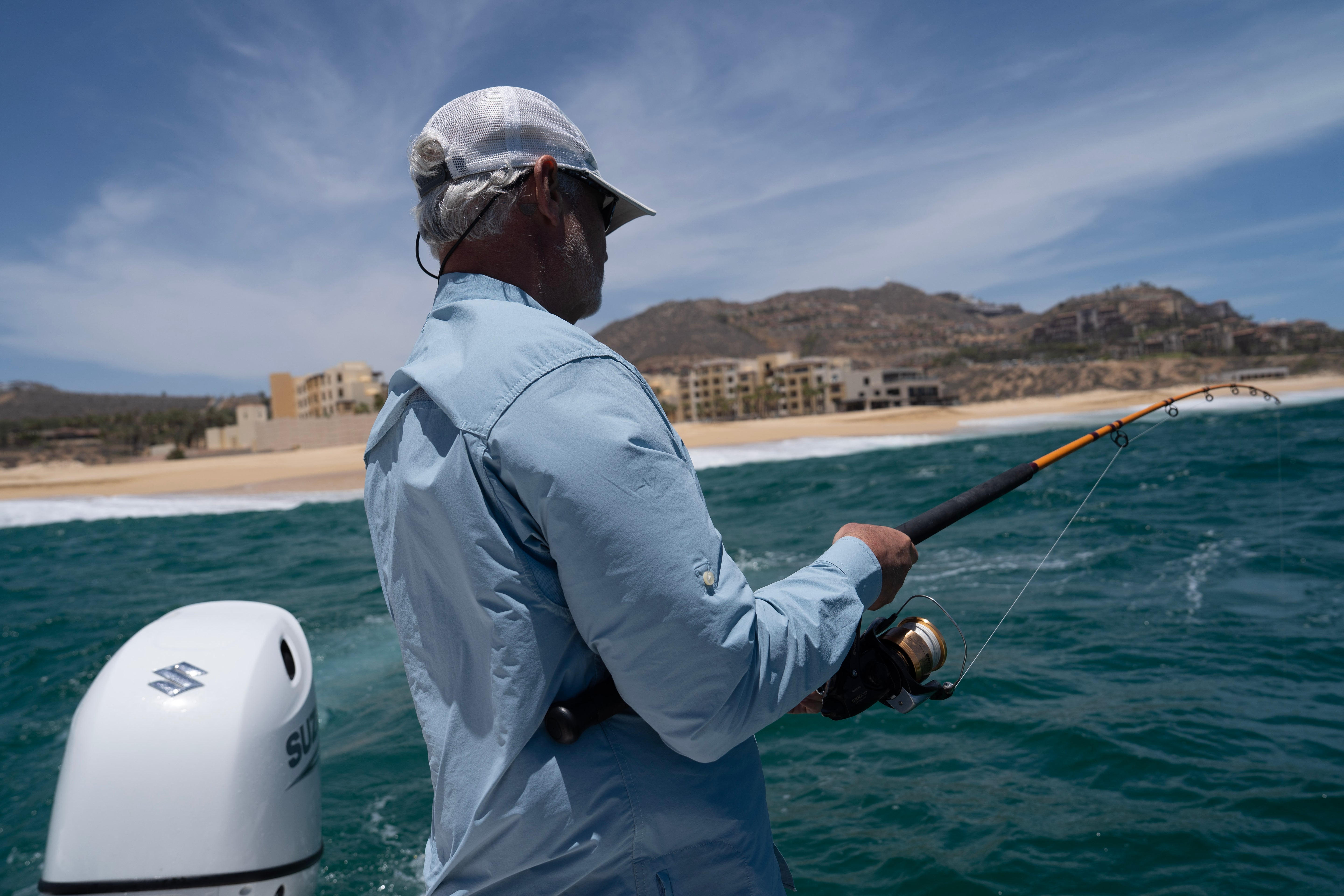 Man fishing on a boat with a scenic background of beach and buildings.