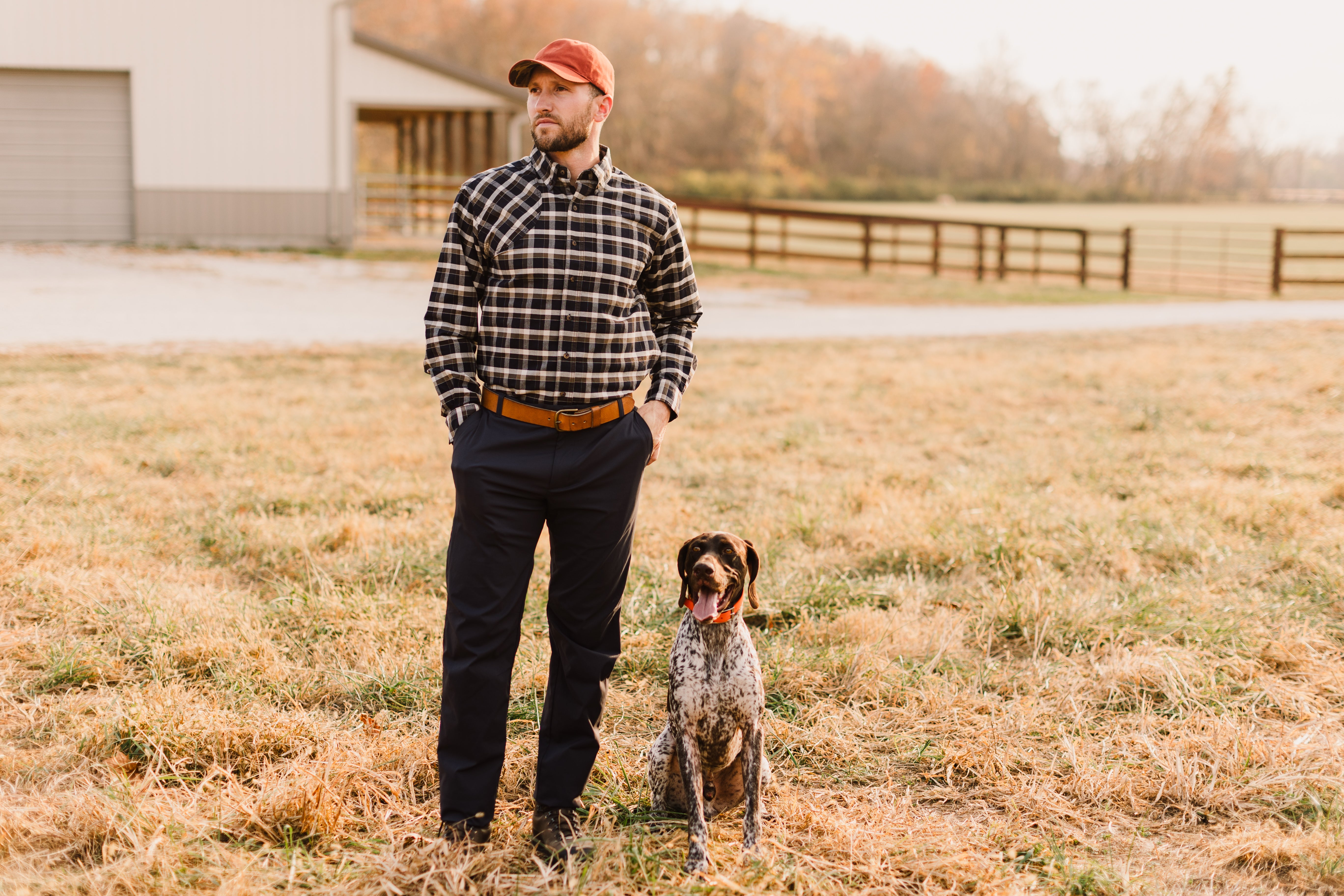 Man in plaid shirt and cap with a dog in a field