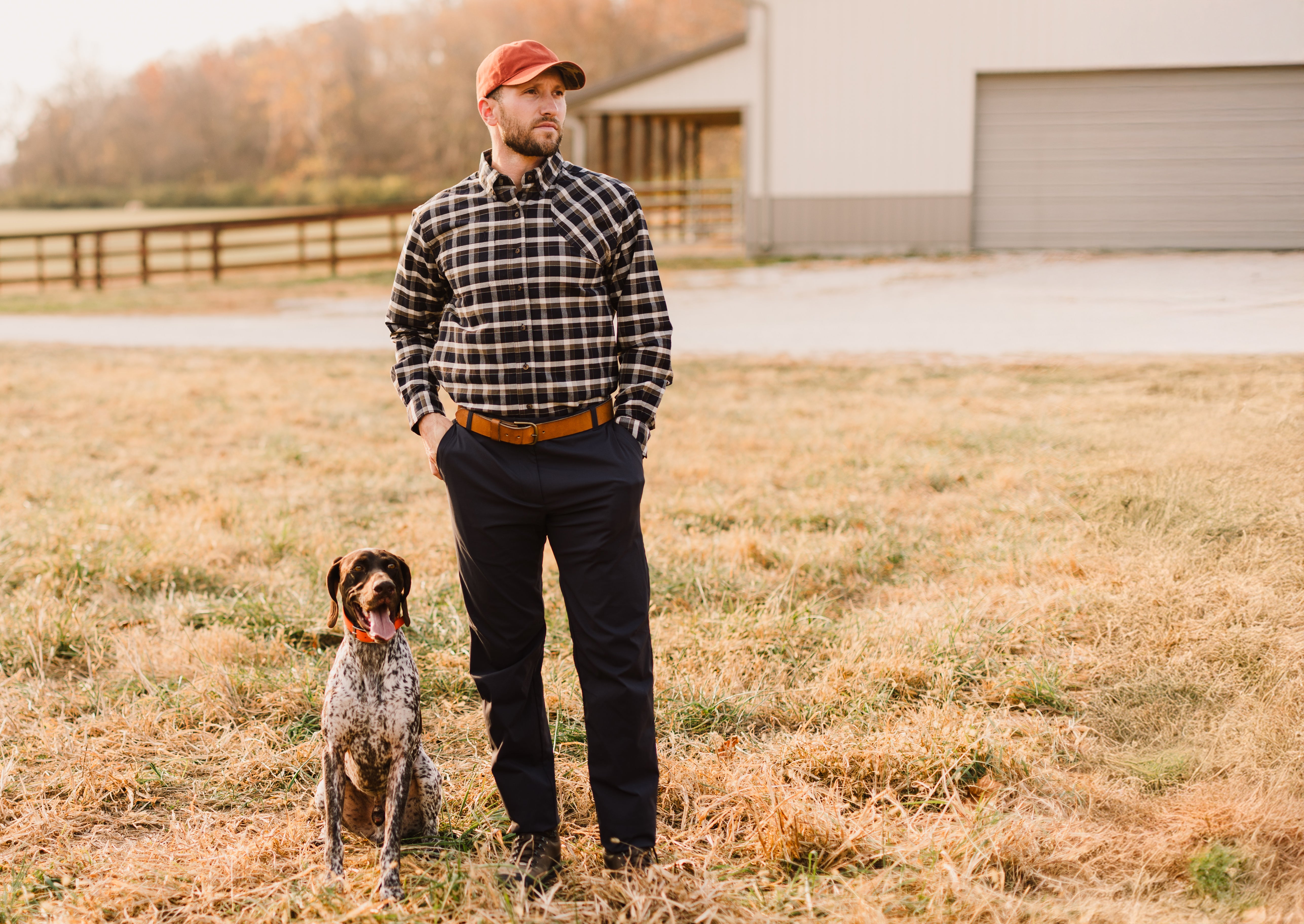 Man in plaid shirt and cap with a dog in a field