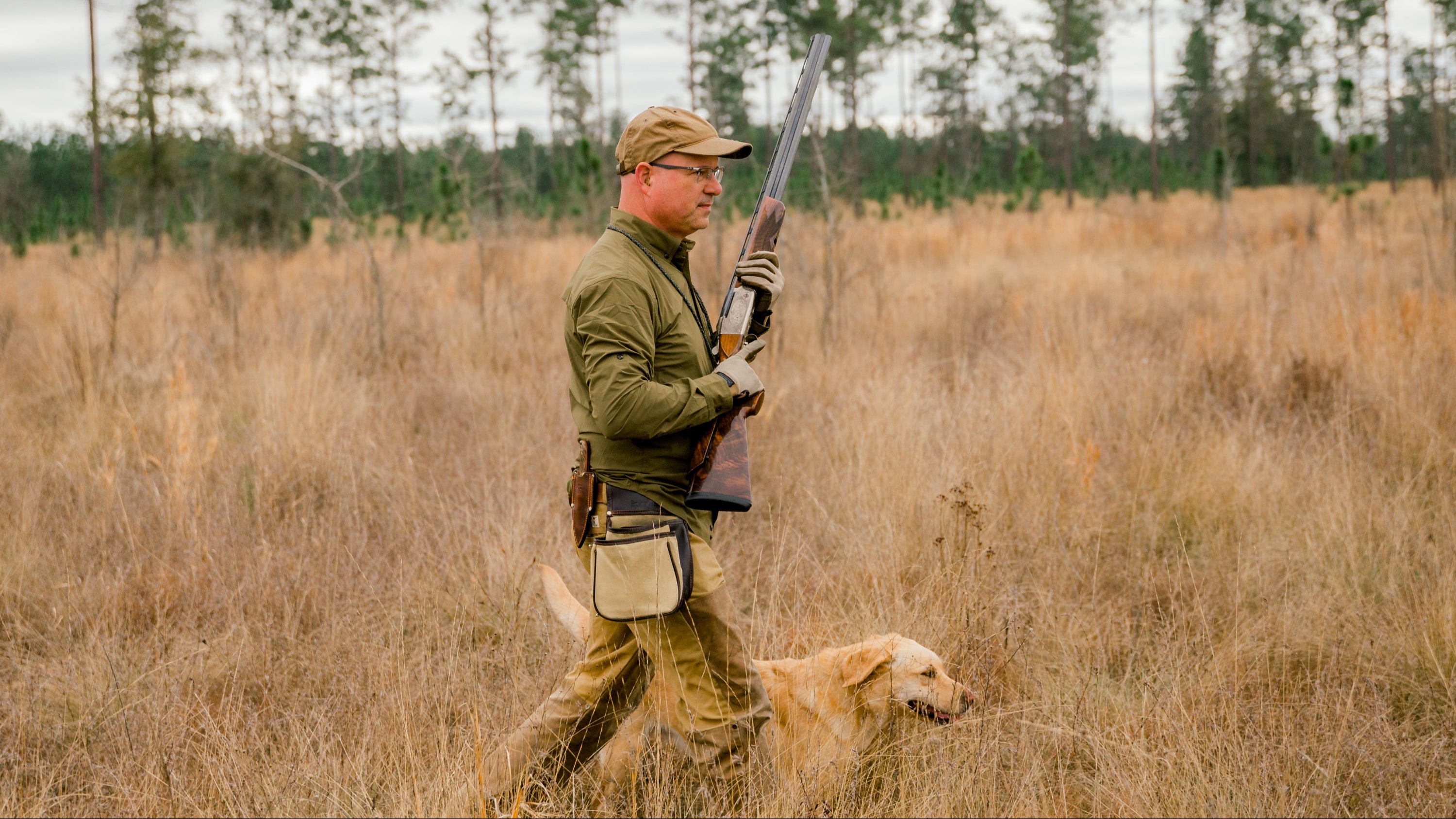 Hunter with a rifle and dog walking through a field