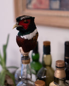 Decorative bird on a bottle with bottles and a painting in the background