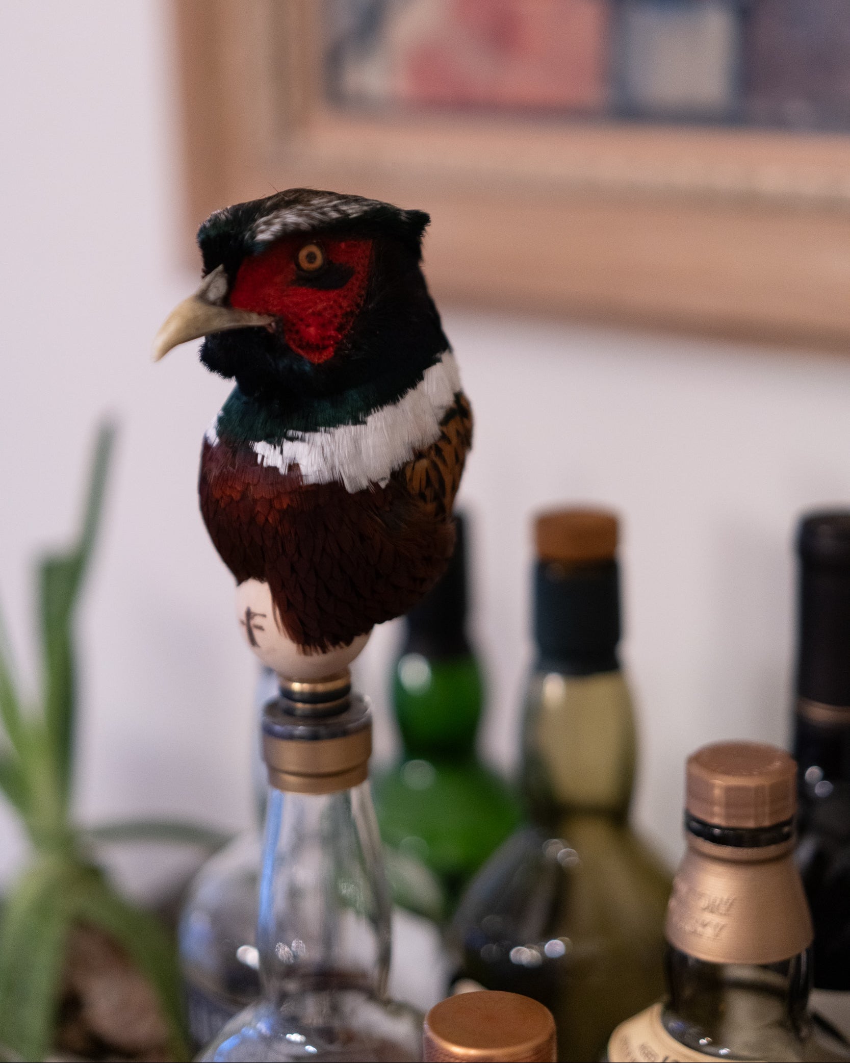 Decorative bird on a bottle with bottles and a painting in the background