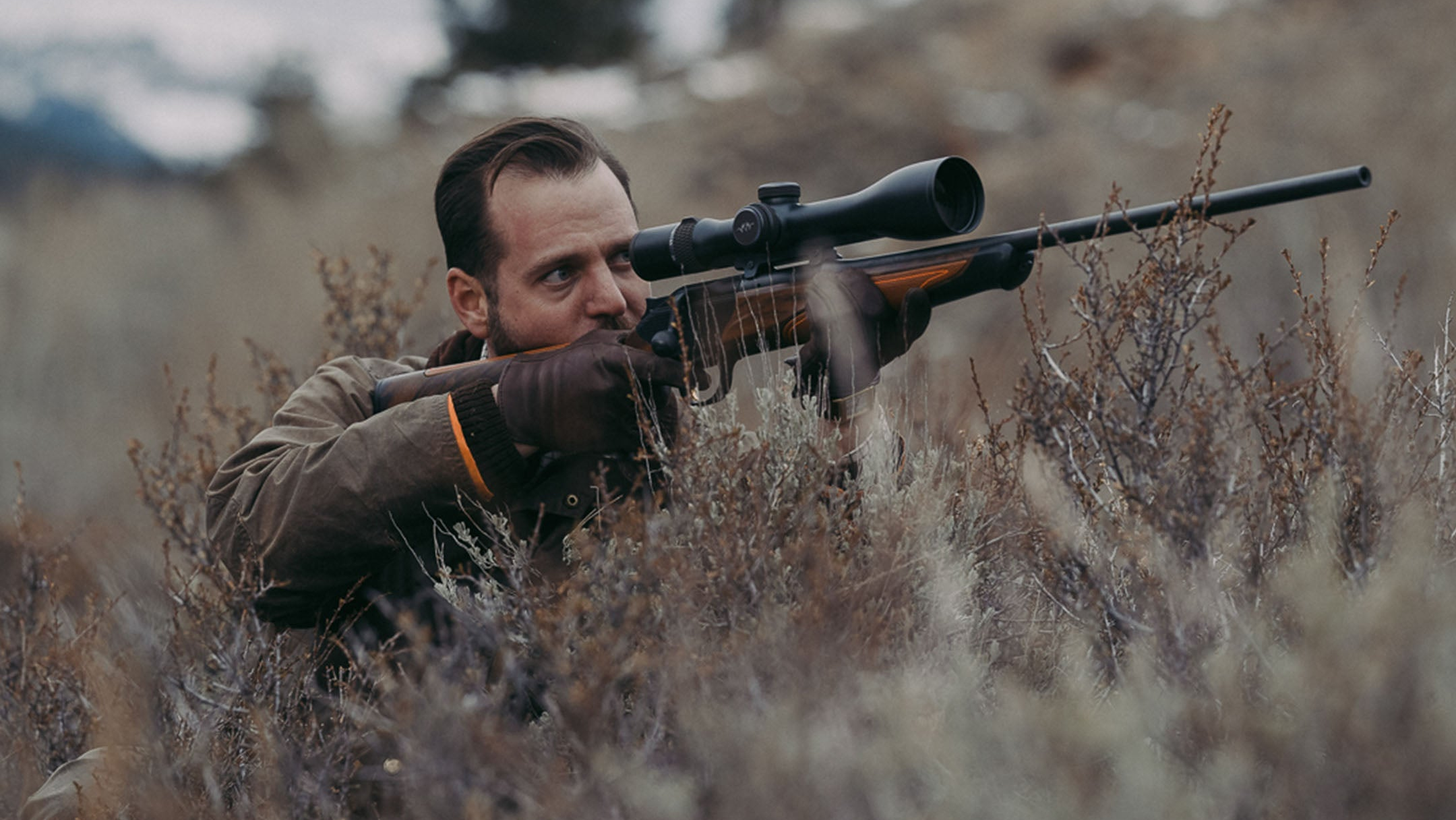 Man in camouflage aiming a rifle with a scope in a natural setting
