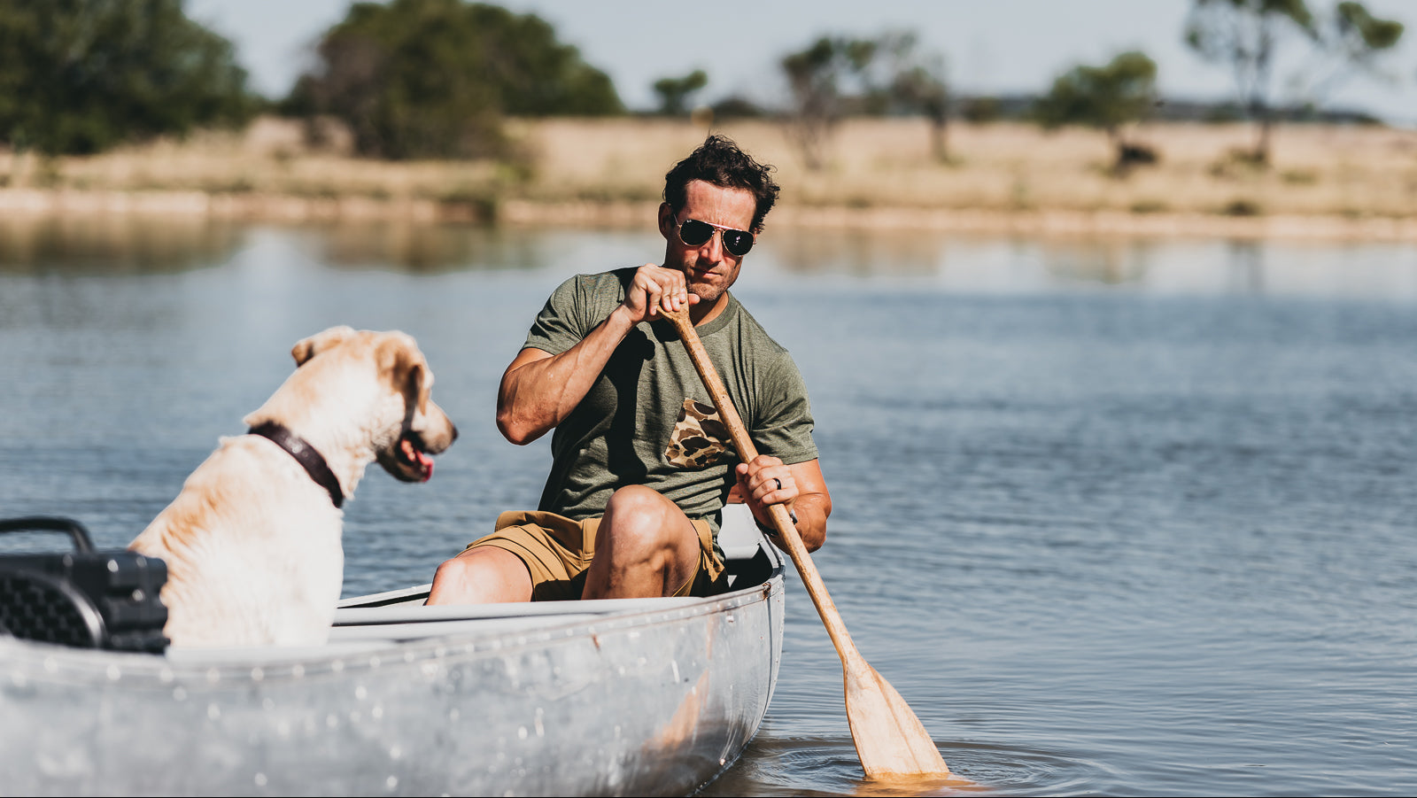 Man paddling a canoe with a dog on a calm lake