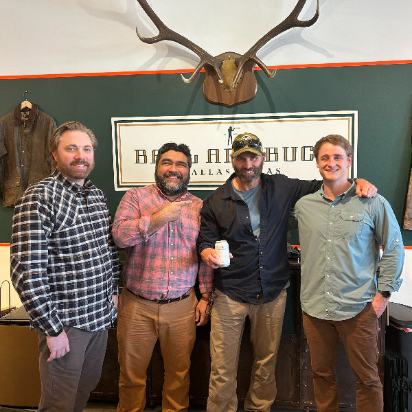 Four men posing together in a room with hunting-themed decor, including elk antlers on the wall.