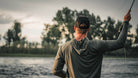 Man fly fishing by a body of water with trees in the background