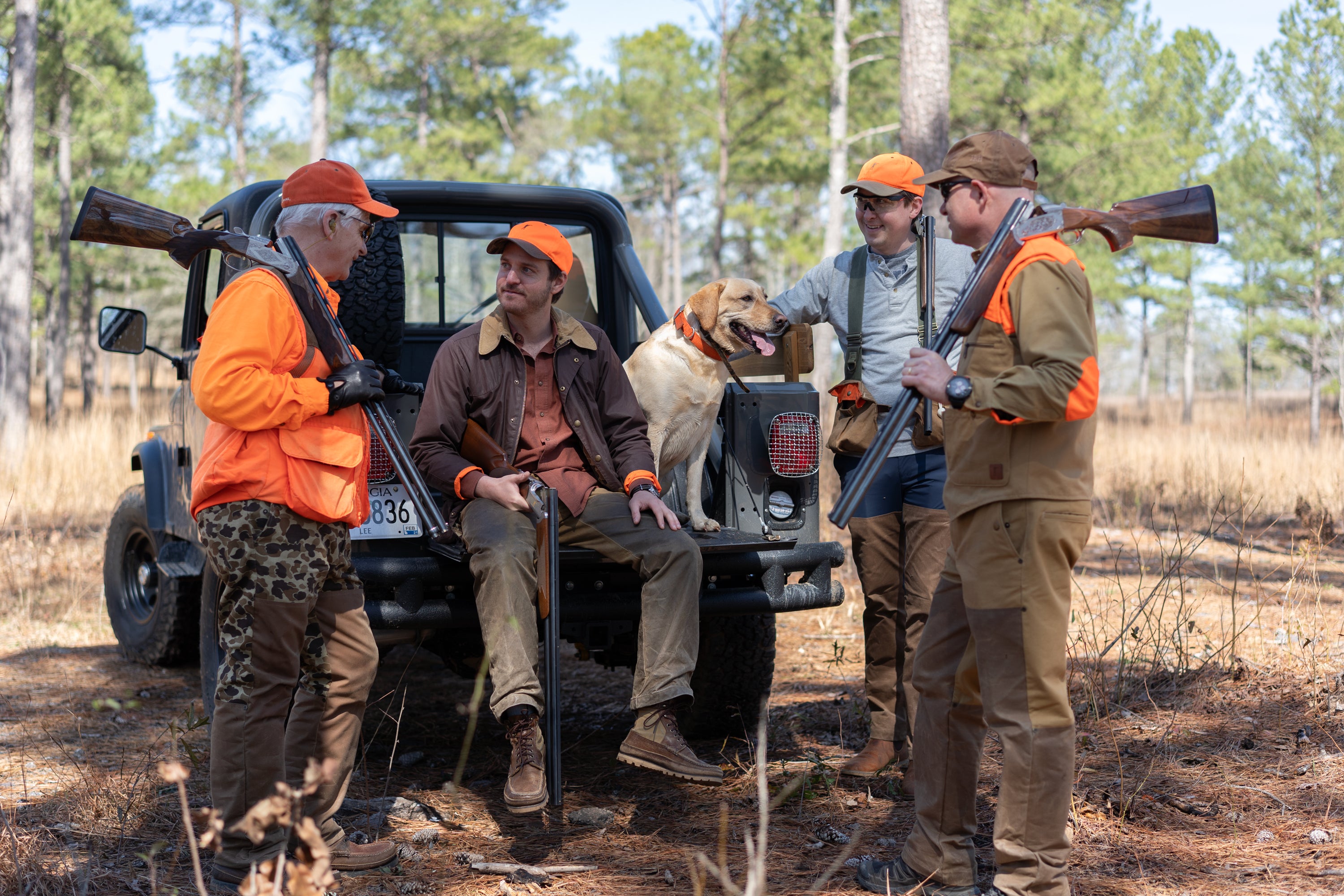 Four hunters with a dog near a vehicle in a wooded area