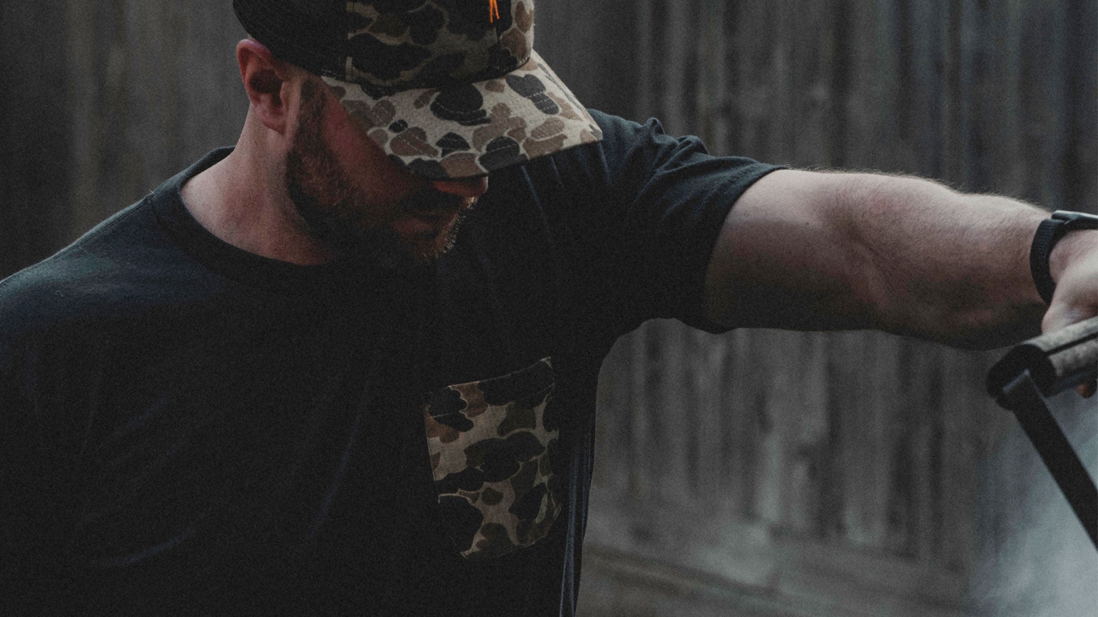 Man wearing a black t-shirt with camouflage design, standing indoors.