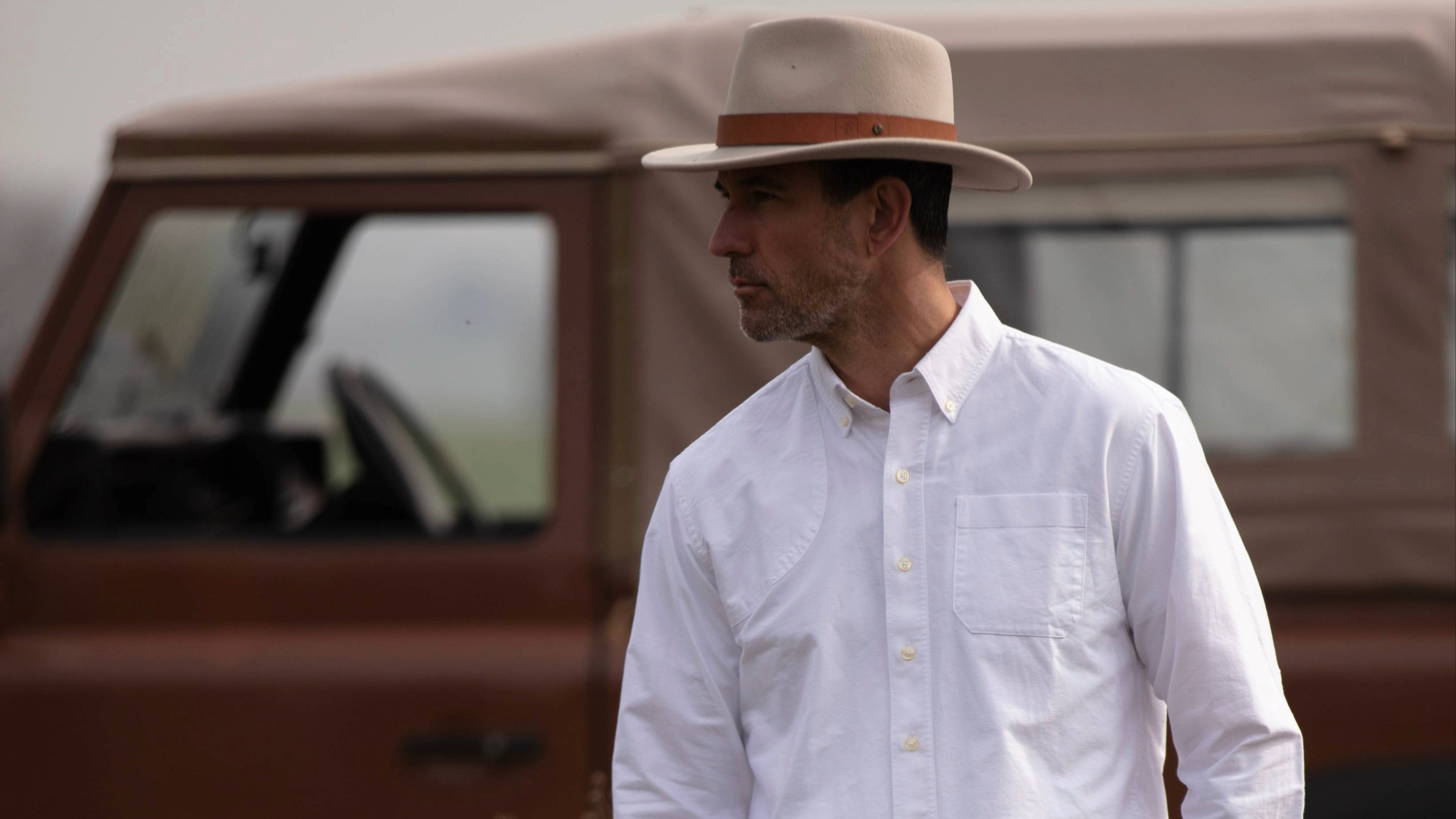 Man wearing a white shirt and hat standing in front of a vintage truck.