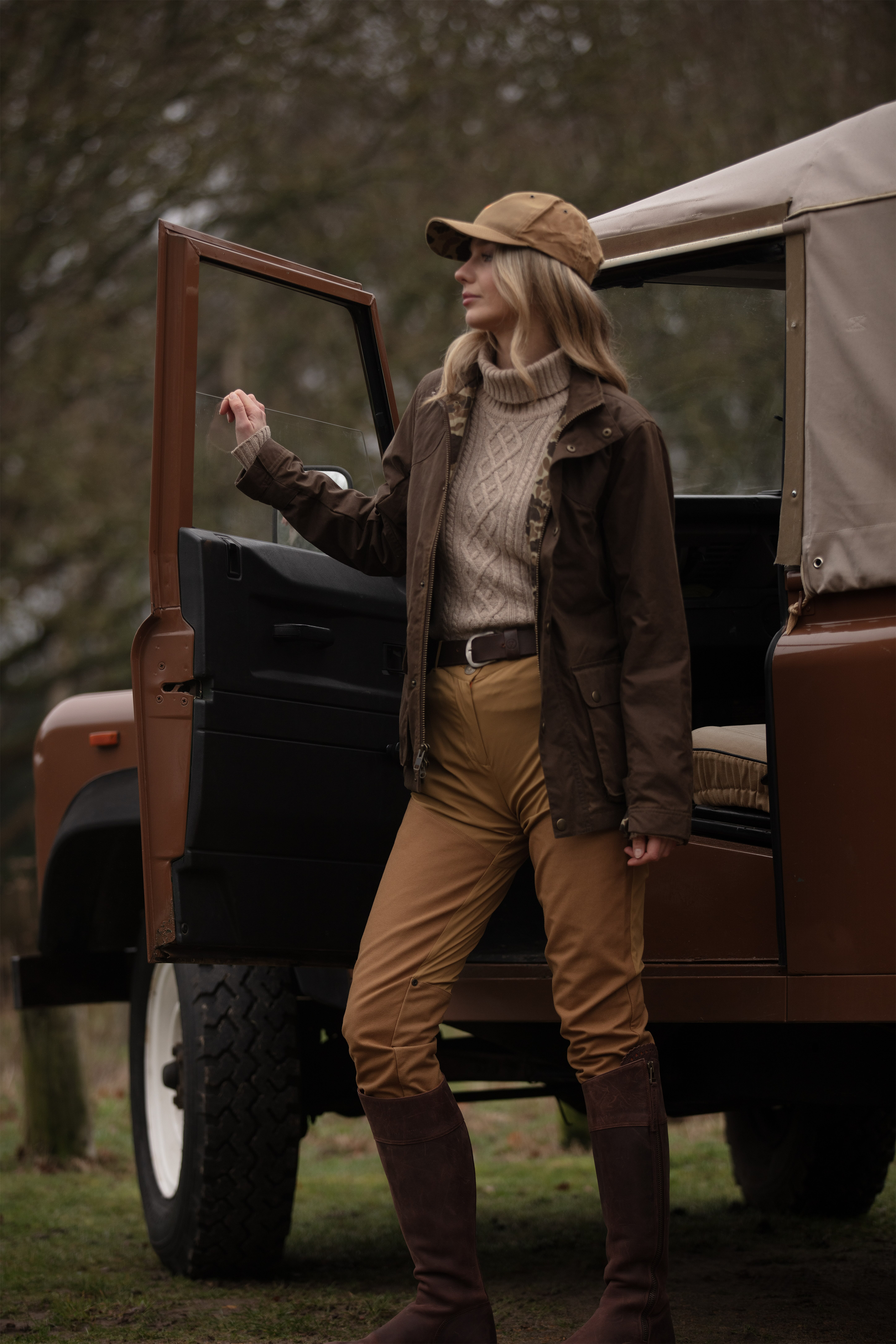 Woman in outdoor attire standing next to a vehicle in a natural setting