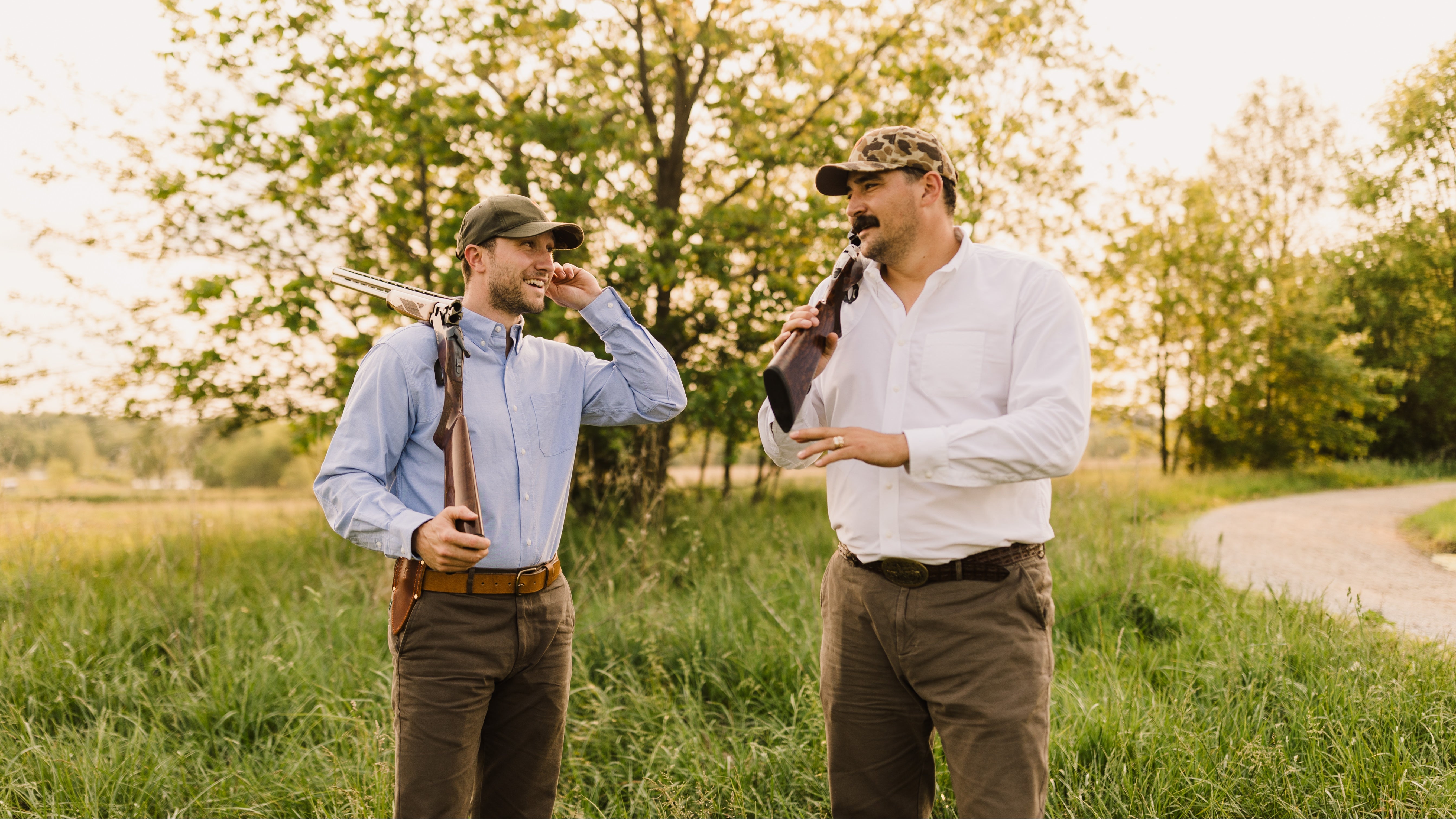 Two men standing in a grassy field with trees in the background