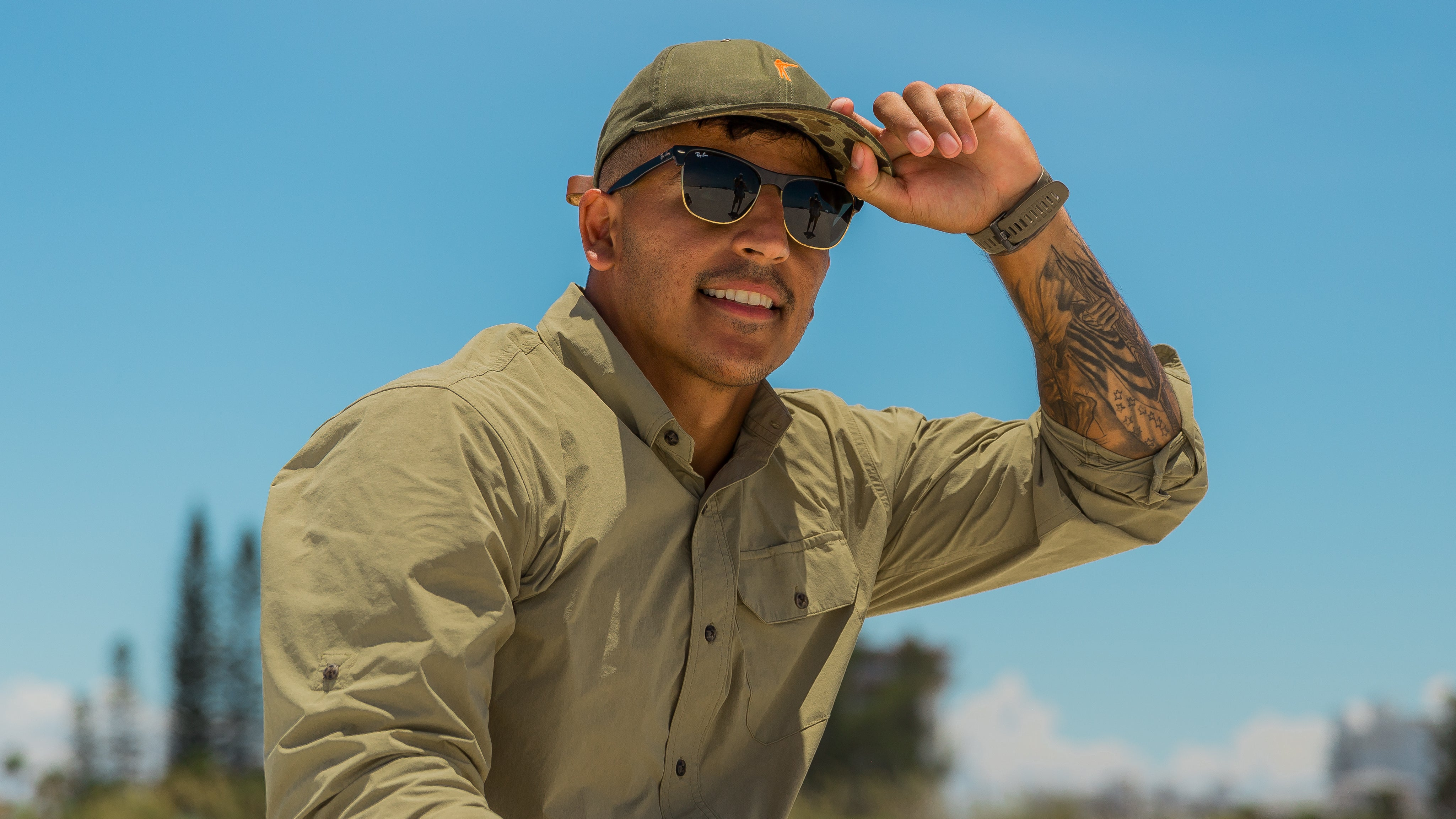 Man wearing a green cap and sunglasses outdoors with a clear blue sky.