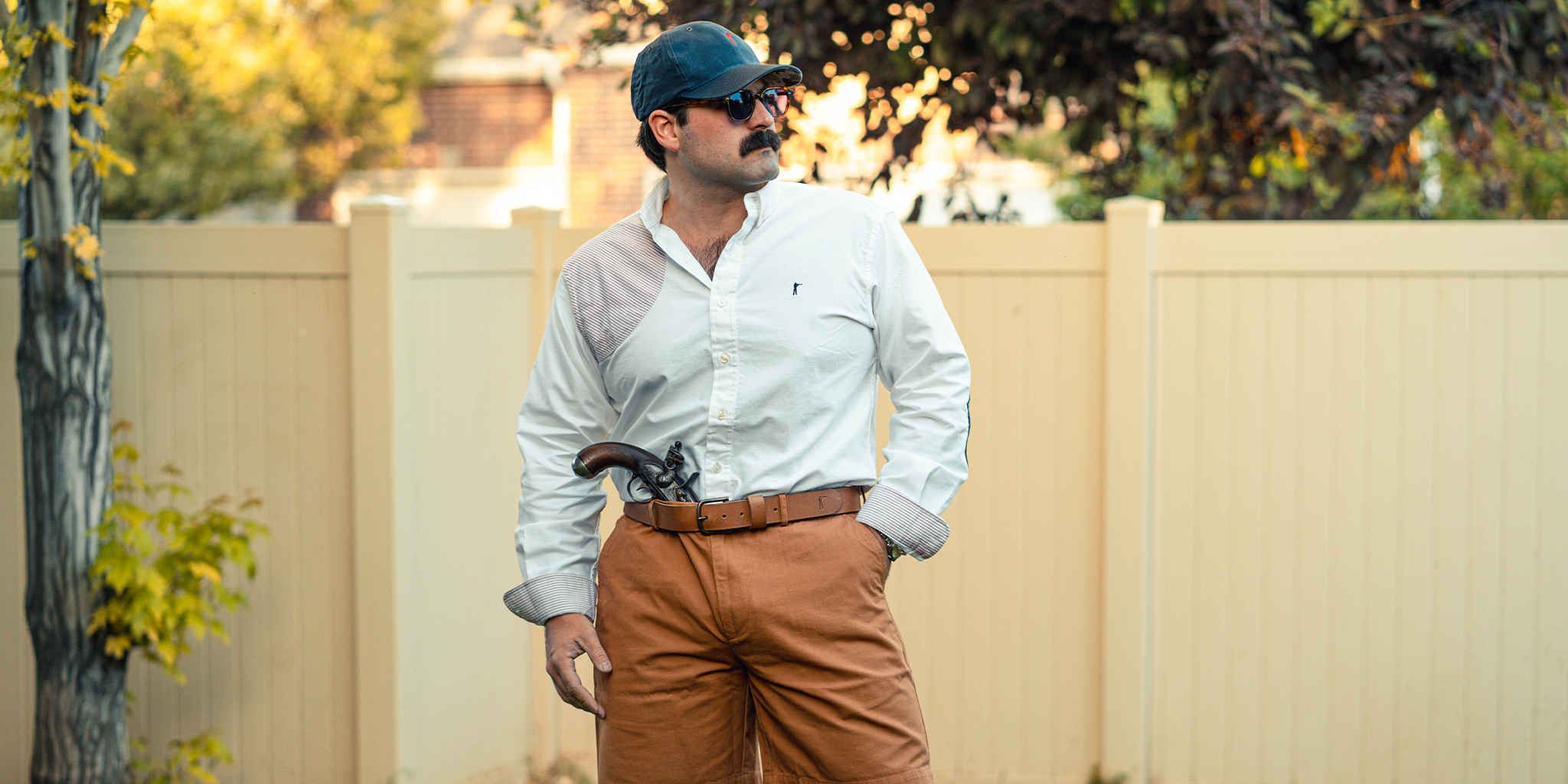Man wearing a white shirt and brown pants standing outdoors with a neutral background