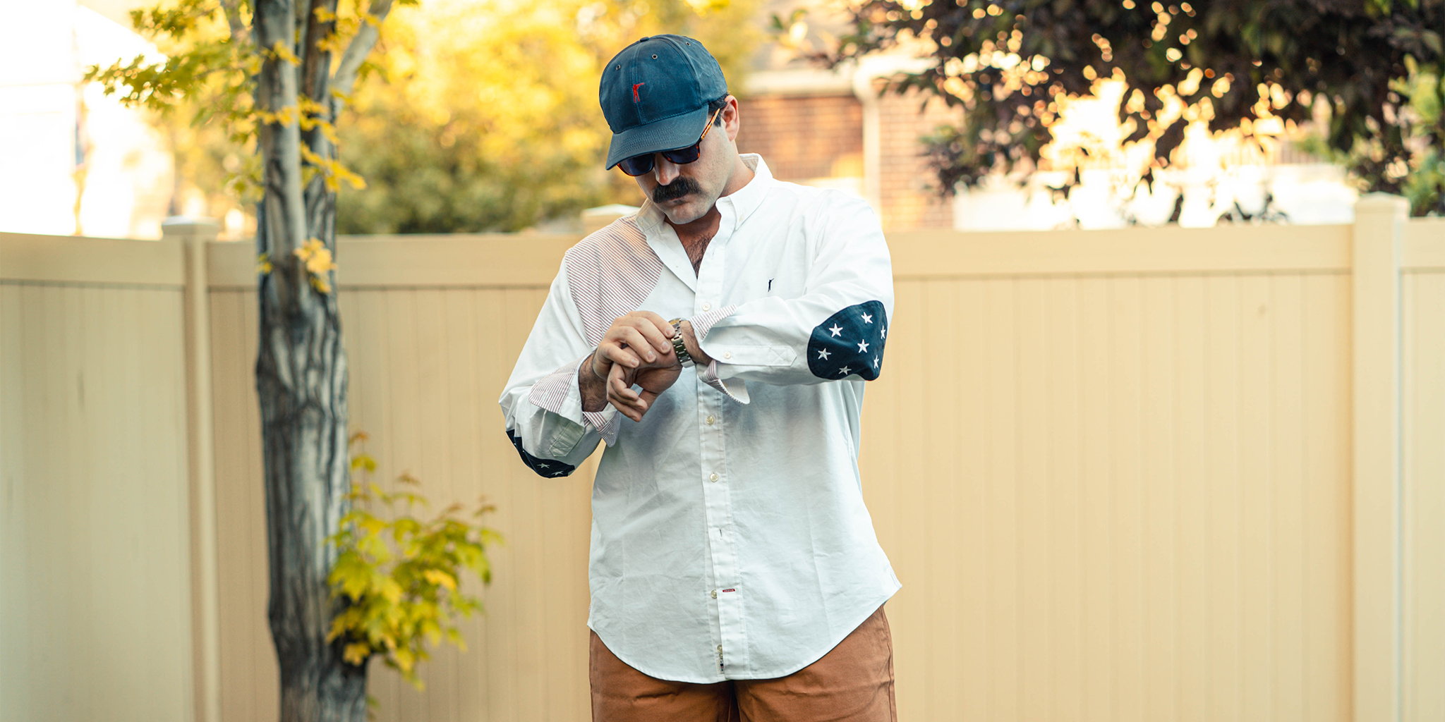 Man in a white shirt and cap holding a skateboard outdoors.