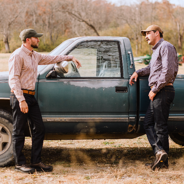 Two men standing next to a green pickup truck in an outdoor setting.