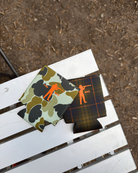 Two can coolers with camouflage and plaid patterns on a white surface.