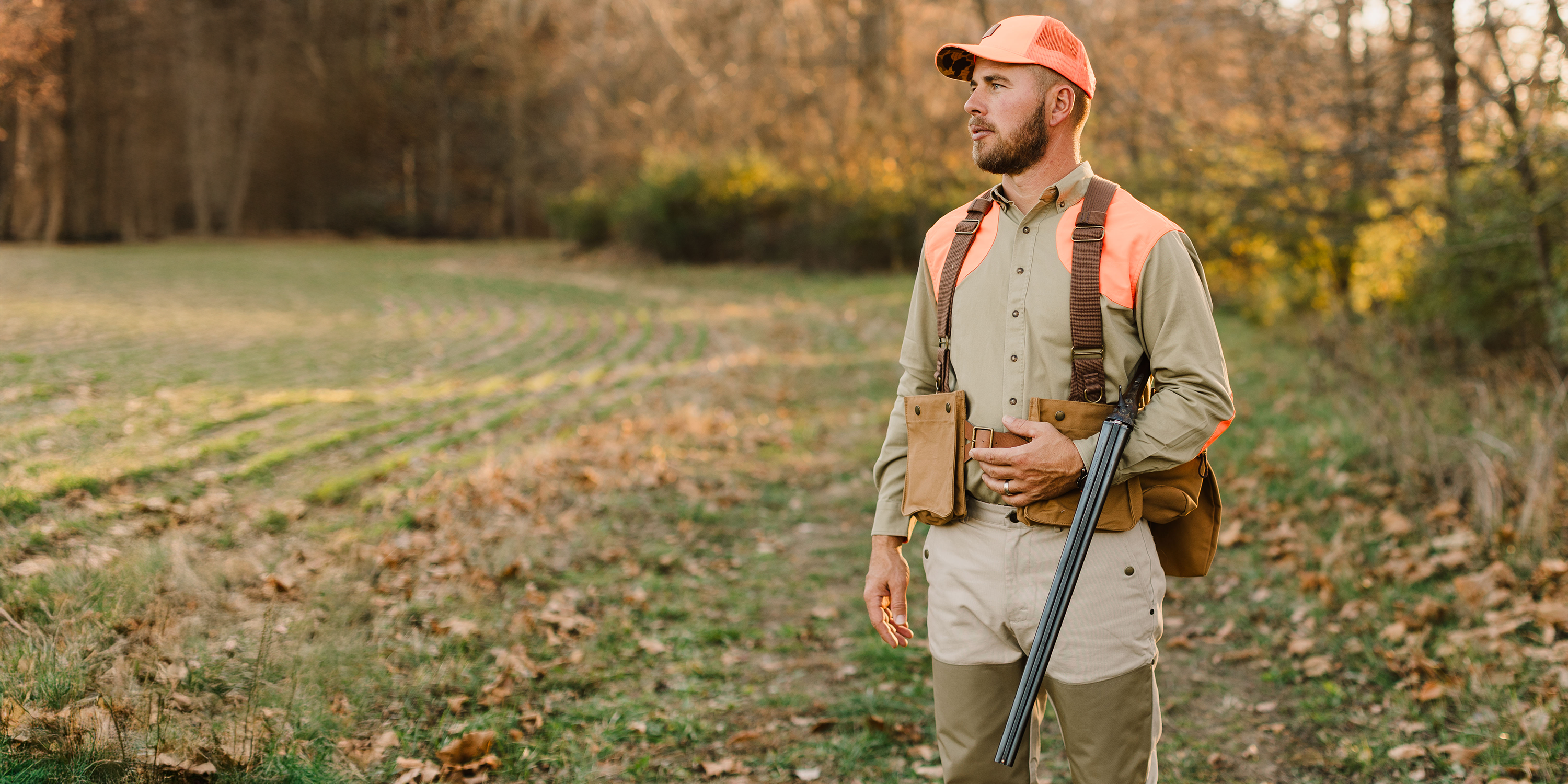 Man in hunting attire with a rifle and binoculars in a forest setting